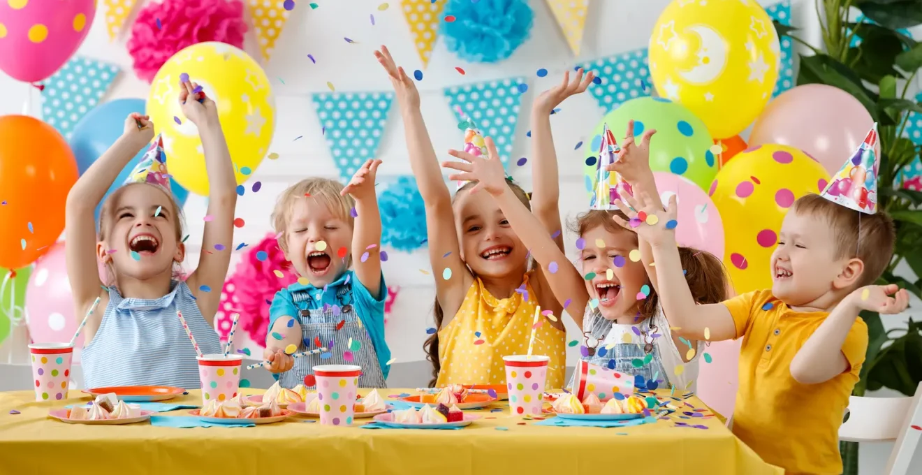 Des mains d'enfants partagent un gâteau d'anniversaire sur une table lumineuse.